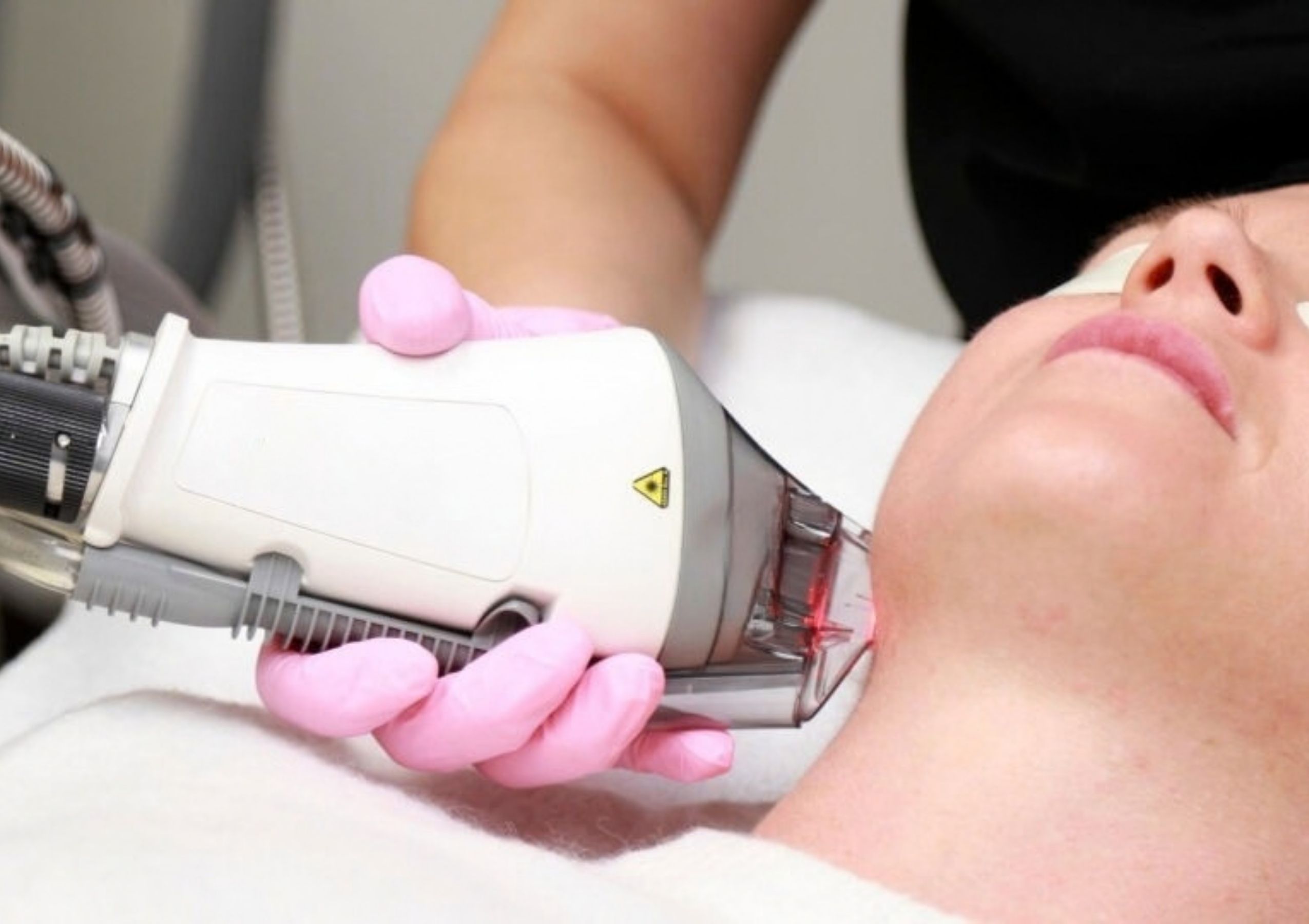 Close-up of a gloved technician using a handheld cosmetic device near a client's eye as the person lies resting.